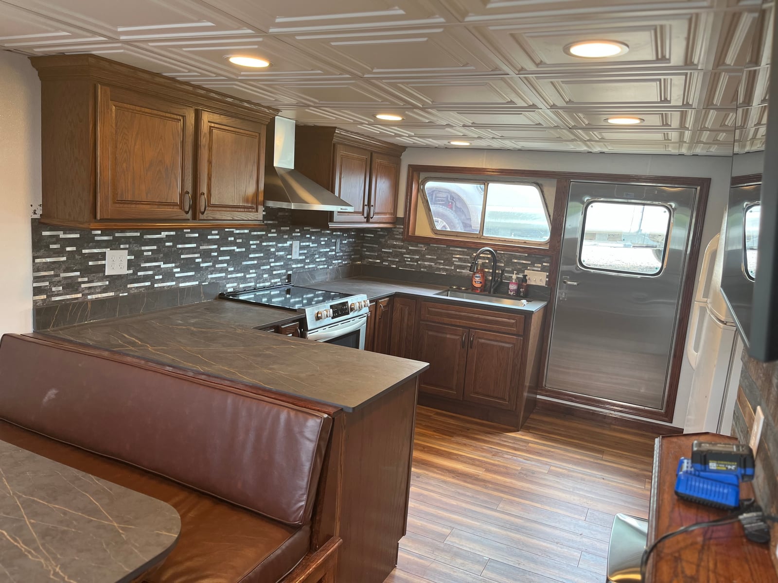 A towboat galley with wooden cabinets, a stove, sink and brown upholstered bench seating.