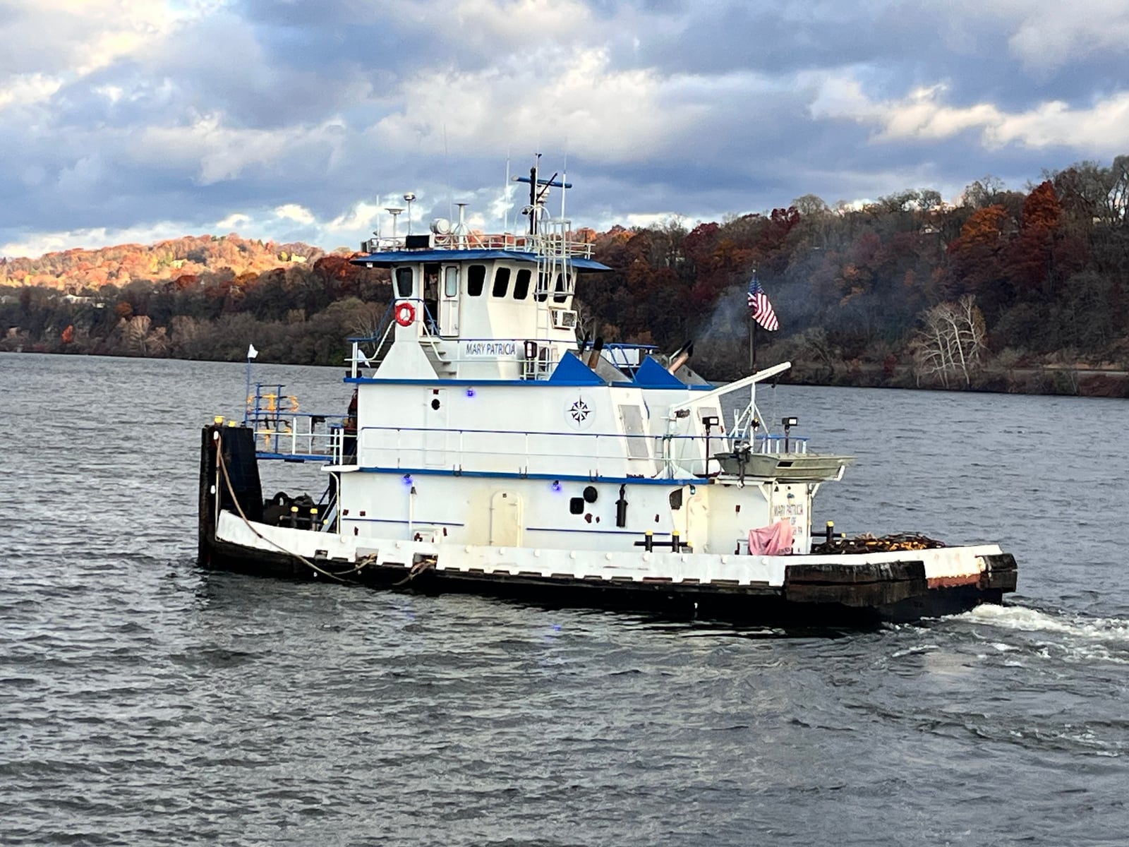 Mary Patricia underway on the river beneath a cloudy sky, with autumn trees along the far bank.