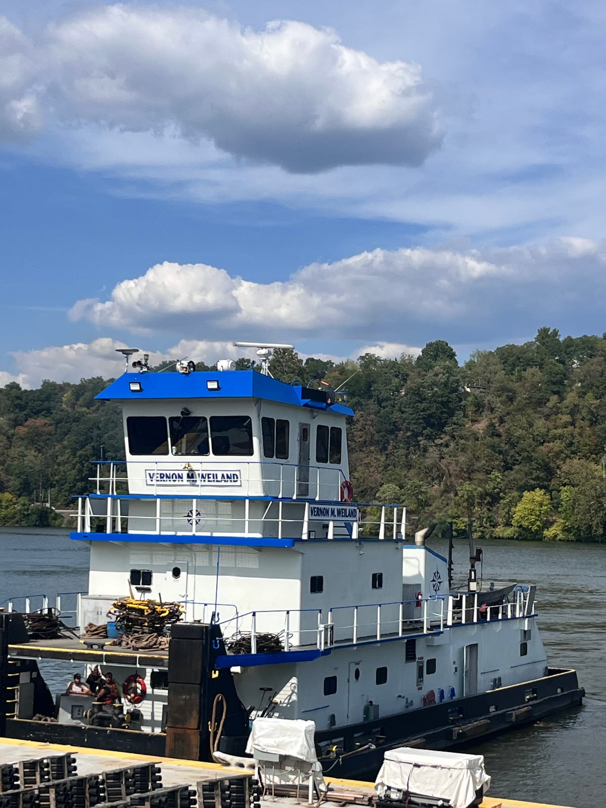 Vernon M. Weiland moored at the riverbank beneath a cloudy sky, its name visible below the blue-roofed pilothouse.